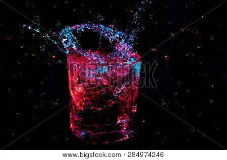 Poured Clear Beverage Under Glowing Colorful Lights Splashing Out From A Full Rocks Glass Isolated O