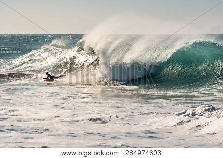 Man Surfing A Huge Wave That Chases Him, The Sunlight Reflects Golden On The Turquoise Surface Of Th