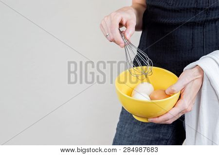 Caucasian Woman With Black Shirt Holding An Eggbeater And A Yellow Bowl Full Of Hen Eggs.