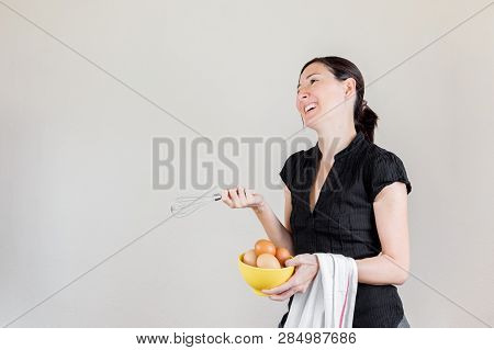 Beautiful Caucasian Woman With Black Shirt Holding An Eggbeater And A Yellow Bowl Full Of Hen Eggs.