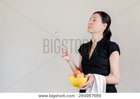 Beautiful Caucasian Woman With Black Shirt Holding An Eggbeater And A Yellow Bowl Full Of Hen Eggs.