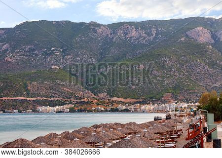 Thatched Peaks Of Beach Umbrellas With Sun Loungers On The Deserted Shore Of The Corinthian Gulf Emb