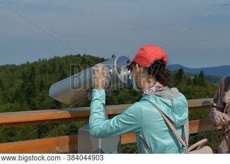 Teeneger Girl Looking Into The Binoculars At A Lookout Tower At The Surrounding Trees