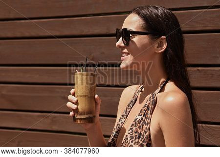 Happy Woman Enjoying Exotic Drink In Bar, Looking Smiling In Distance, Wearing Black Sunglasses And 