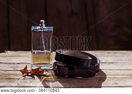 Men's Perfume In A Transparent Dispenser Next To A Black Leather Belt Lie On A Wooden Table With An 