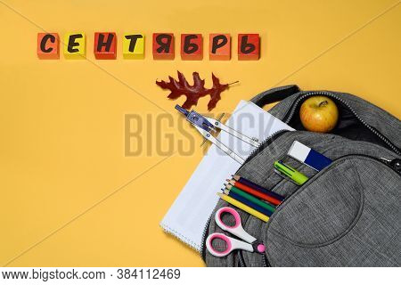School backpack with compasses, ruler, eraser, pencils, pen, scissors  and apple on yellow background with red leav.Knowledge concept.Back to school. Start to study.Inscription \