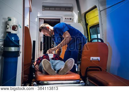 Unconscious Woman Lying On A Stretcher In An Ambulance Car, A Paramedic Providing Her First Aid.