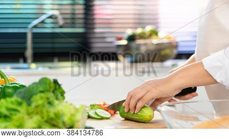 Young Asian Woman Is Preparing Healthy Food Vegetable Salad By Cutting Cucumber For Ingredients On C