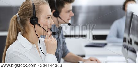 Call Center. Group Of Casual Dressed Operators At Work. Blond Business Woman In Headset At Customer 