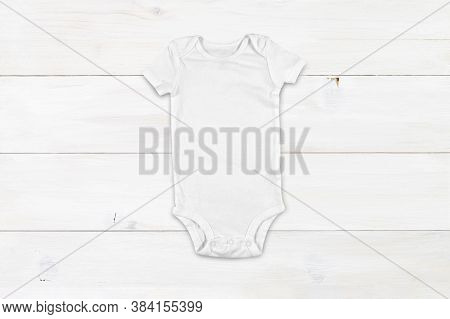 Top Down View Of A White Onesie On A Modern White Wood Background. Plenty Of Space To Add Your Own D