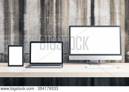 Digital Tablet, Computer Monitor And Laptop With Blank Screen On Office Table On Concrete Wall Backg