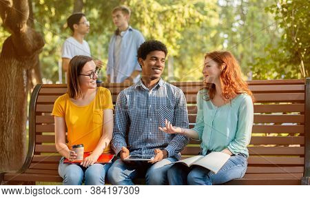 Students Life Concept. Three Diverse Friends Talking Sitting On Bench Outdoors In Park After Univers