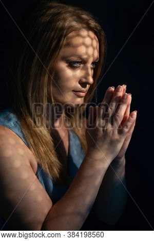 Beautiful woman confesses in the confessional. Praying woman, fine art portrait with interesting ligth and shadow pattern. Absolution. 