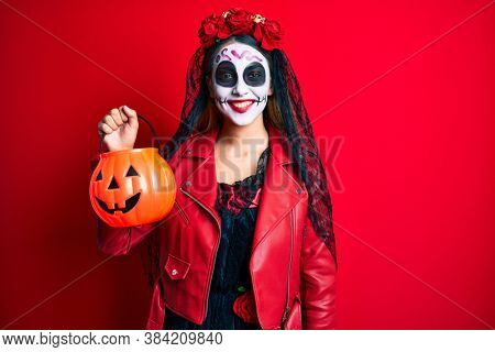 Woman wearing day of the dead costume holding pumpkin looking positive and happy standing and smiling with a confident smile showing teeth 