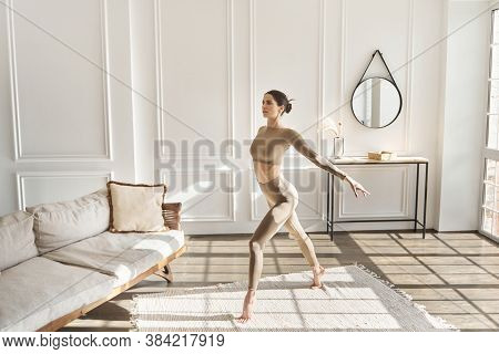 Full Length Portrait Of Beautiful Young Woman Doing Morning Exercises In Living Room, Doing Yoga Or 