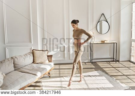 Full Length Portrait Of Tall, Slender Young Woman Doing Morning Exercises In Living Room For Flexabi