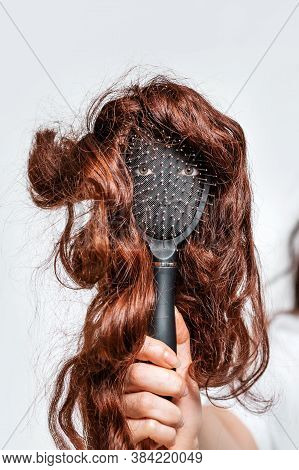 A Womans Hand Holds A Comb With Eyes And A Wig That Imitates A Persons Face. Hair Care Concept