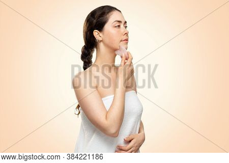 Gua Sha Massage. A Young Woman In A Bath Towel Is Doing A Guasha Massage In The Chin Area. Beige Bac