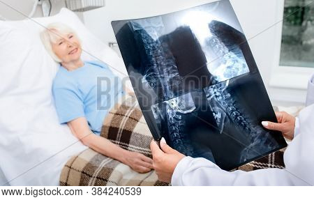 Experienced Doctor Is Holding An X-ray Of The Cervical Spine Of Elderly Woman. Treatment Of Spine Di