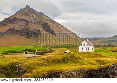 Arnarstapi, Iceland- 26 August 2015: A White Traditional House In A Small Town. Mountains Around.