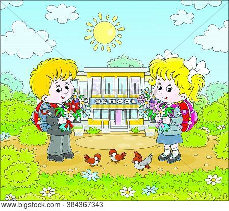 Happy Schoolchildren With Colorful Bouquets Of Flowers And Schoolbags Standing In Front Of Their Sch