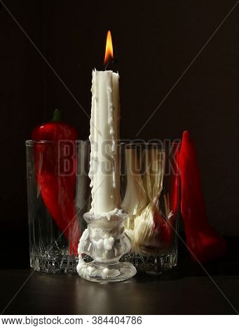 Still Life With Candlestick With Burning Candle, Red Ramiro Peppers And Garlic Bulb In The Glass Bea