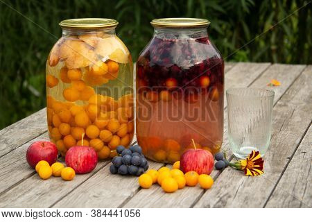 Two Jars Of Plum And Grape Compote Stand On A Wooden Table On The Street. Home-made Preparations For