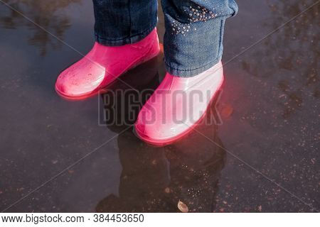 Legs Of Child In Rainboots Standing In Puddle.kids In Fall. Close-up Of A Baby Girls Legs With Pink 