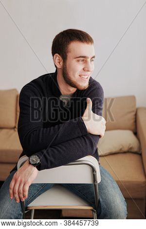 Handsome Man Wearing A Black Jacket And Jeans Sitting Down Intside