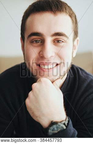 Handsome Man Wearing A Black Jacket And Jeans Sitting Down Intside