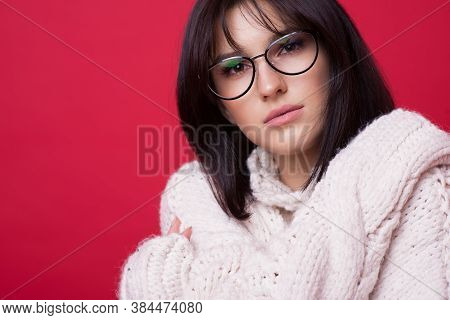 Close Up Photo Of A Caucasian Brunette Woman With Eyeglasses Posing In A Warm Sweater On A Red Studi