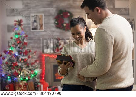 Happy Girlfriend About Her Christmas Gift From Boyfriend And Christmas Tree In The Background.