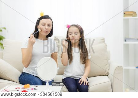 Mother And Daughter Are Doing Make Up And Having Fun Sitting At Dressing Table At Home.