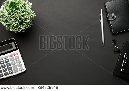 Top view of modern black office desk with calc, notebook, pen and a lot of things. Flat lay table layout. Copy space for text.