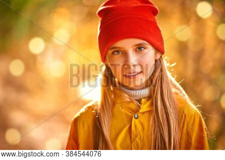 Cute child girl  in red hat and yellow cloak looks at the camera and smiling. Autumn fashion for children.
