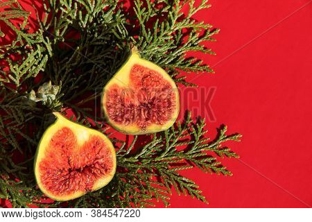 Fig Halves On A Red Background With A Plant. Fig Slices With Thuja.