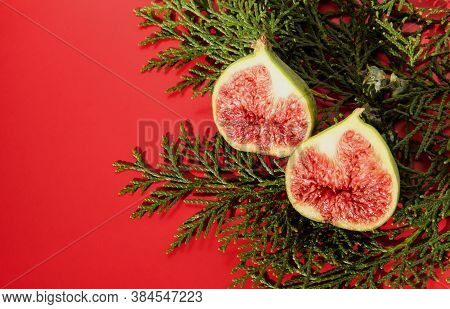Fig Halves On A Red Background With A Plant. Fig Slices With Thuja.