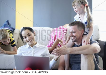 Man And Woman And Their Children Are Smiling And Laughing While Sitting On Floor And Looking At Lapt