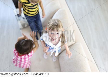 Boy And Girls Laugh And Jump On Couch At Home. Home Games For Children Concept