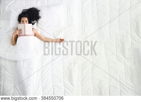Woman Lies On White Bed With Closed Eyes Book Lies On Her Face. Relax And Tranquility Before Bed Con