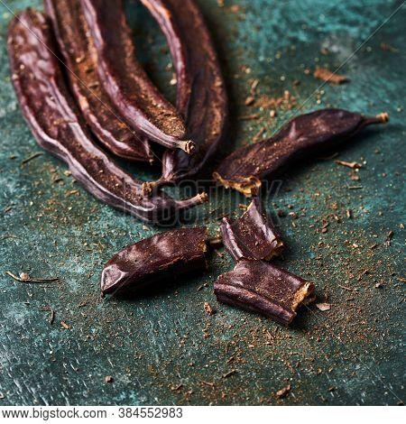 closeup of some ripe carob beans on a rustic dark green surface