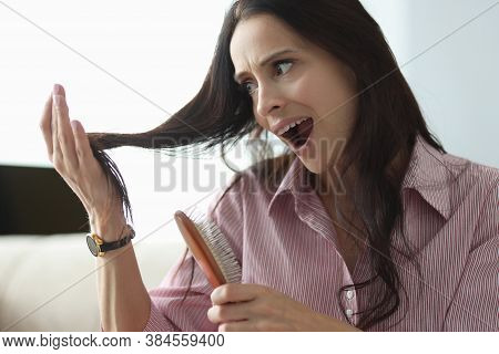 Woman Holds Comb In Her Hand And Looks At Her Hair In Panic. Hair Loss In Women Concept