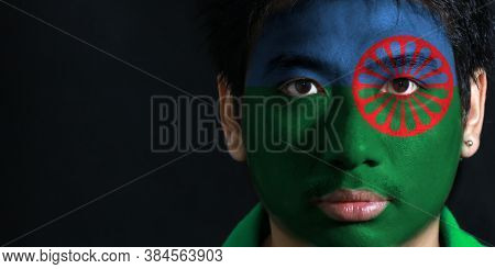 Portrait Of A Man With The Flag Of The Romani People Painted On His Face On Black Background. Blue A