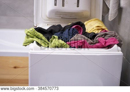 Hand Holds A Gel Pod For Washing On The Background Of A Washing Mashine With Underwear