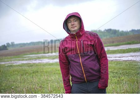 A Guy In A Red Jacket With A Hood Stands Under A Rainy Sky