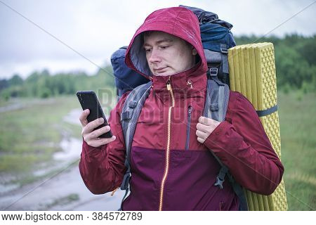 Hiker Traveler With A Large Backpack Is Looking At A Map In His Smartphone.