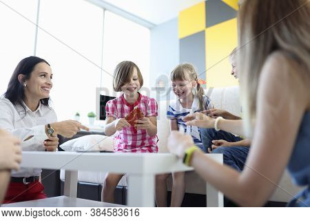 Adults And Children Are Sitting Around Table Holding Game Cards And Laughing Merrily. Positive Commu