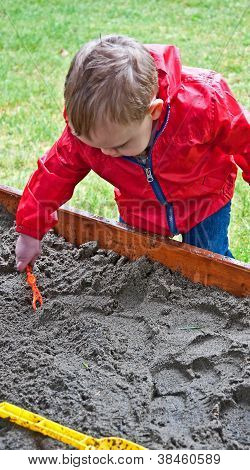 Toddler Boy Playing In Sand Box On Rainy Day
