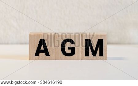 A Wooden Block With The Word Agm Annual General Meeting Written On It On A White Background.