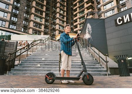 Active Old Woman Riding Electric Scooter. Retired Lady Uses Environmentally Friendly City Vehicle. G